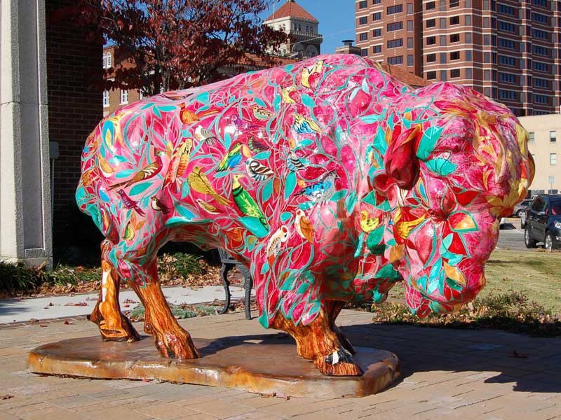 Colorfully painted buffalo sculpture in reds, pinks, turquoise leafs with birds hidden in design.  